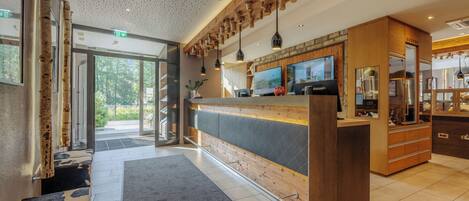 A modern reception area with a wooden reception desk, a large flat-screen TV, and a seating area with a patterned rug.
