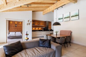 Interior moderno com sofá, mesa de jantar, cozinha e cama com cabeceira de madeira.
