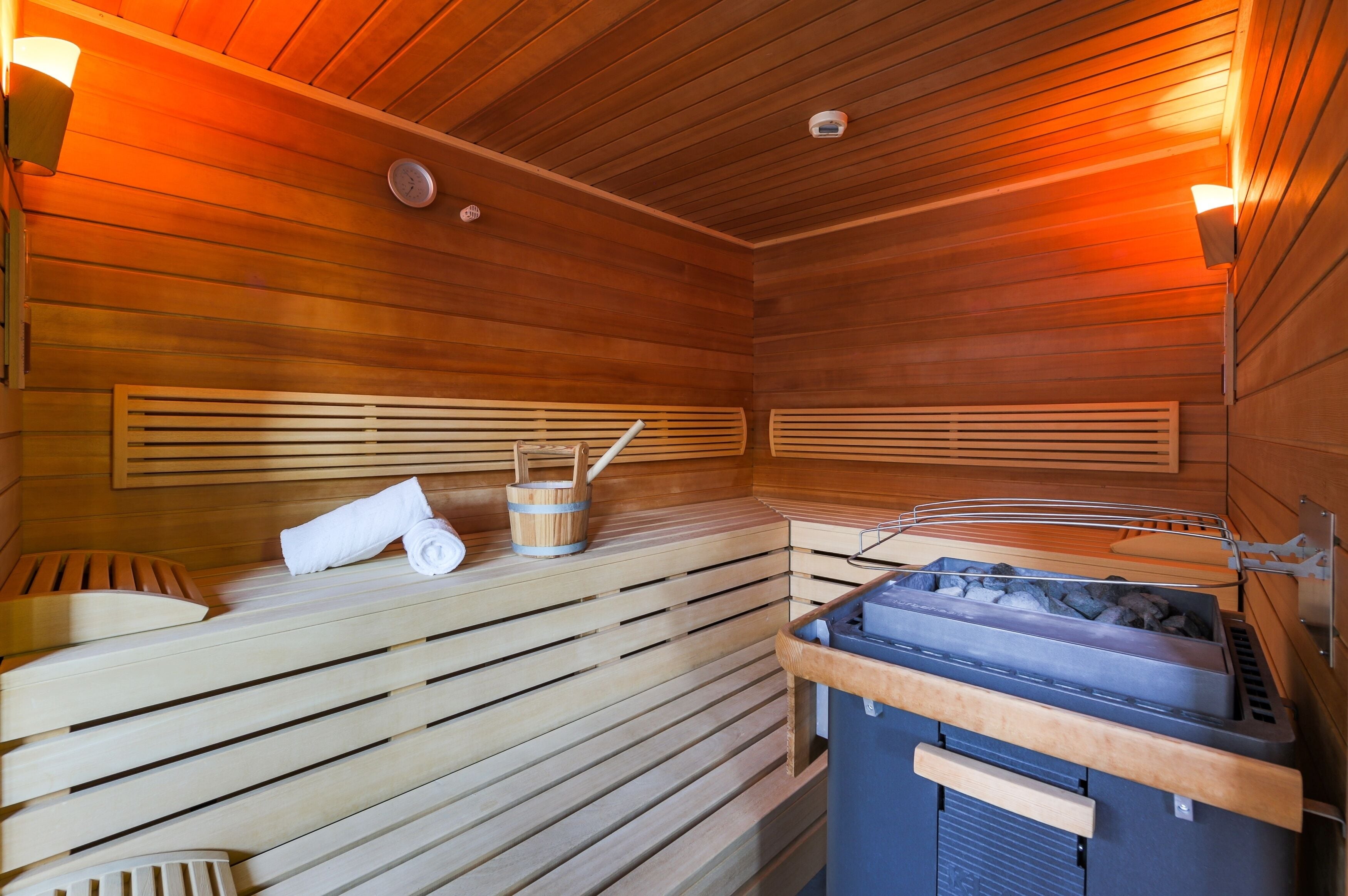 A sauna with wooden benches, a towel, a bucket, and a steam generator.