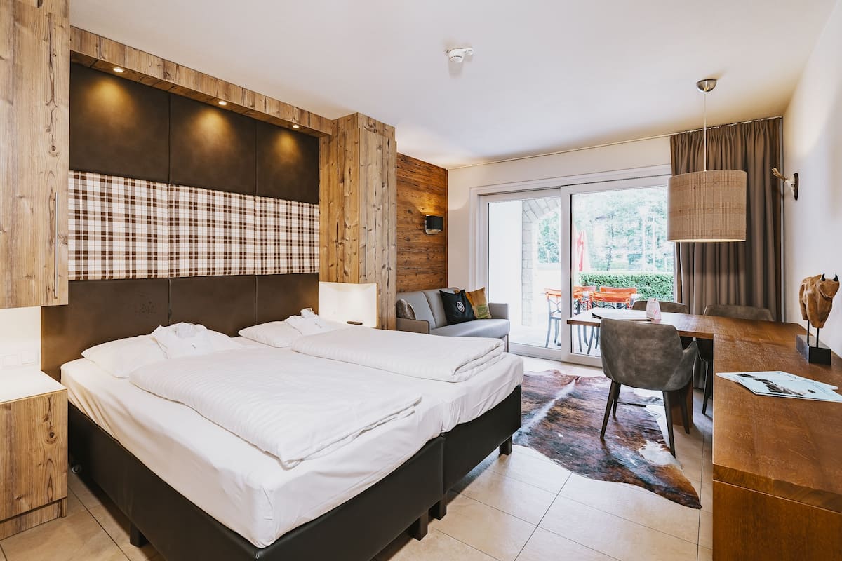 A modern hotel room with a large bed, a desk, and a view of the outdoors.