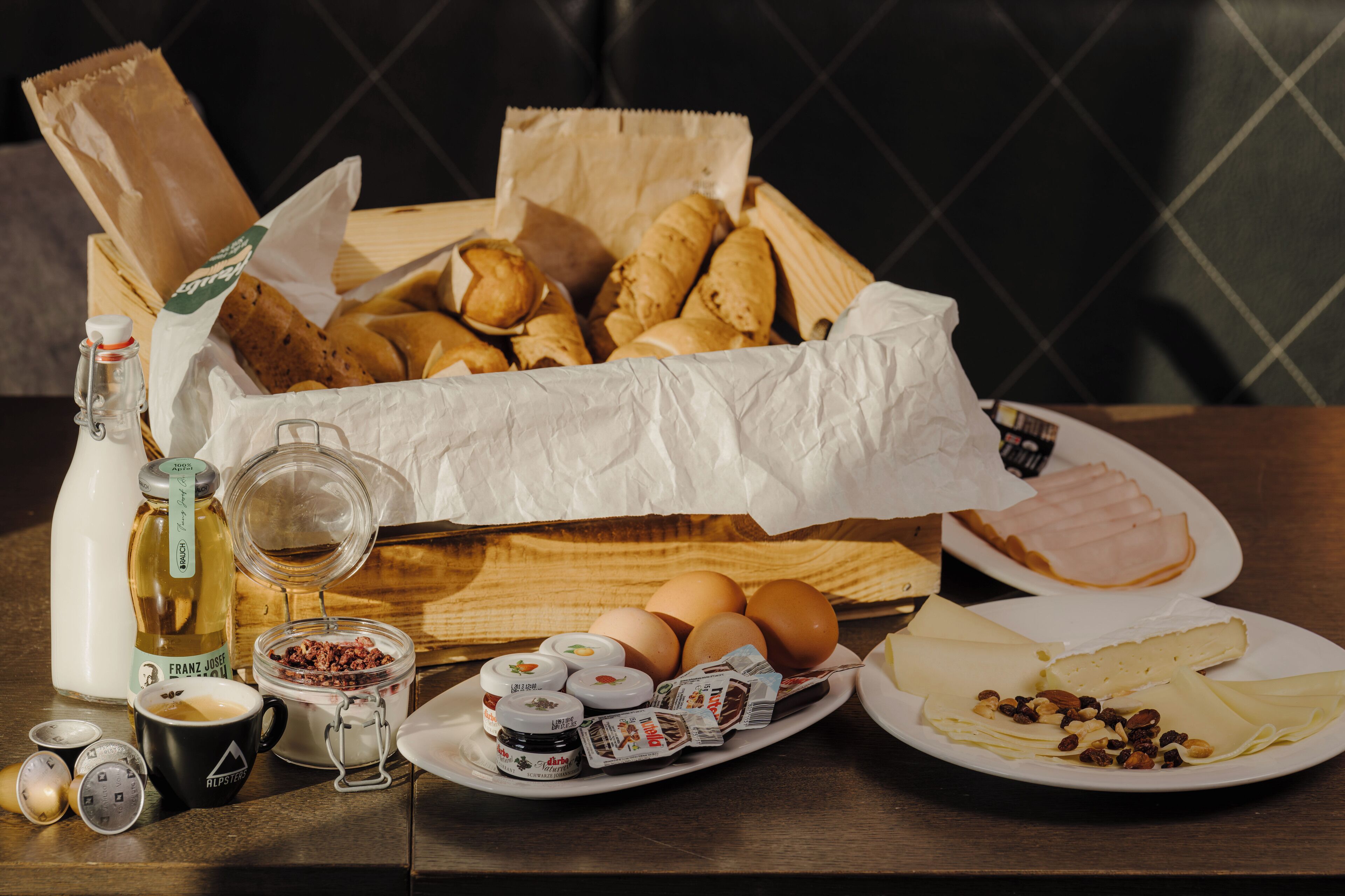 Een houten mand gevuld met brood, een fles Franz Josef, een glas melk, eieren en diverse toevoegingen op een tafel.