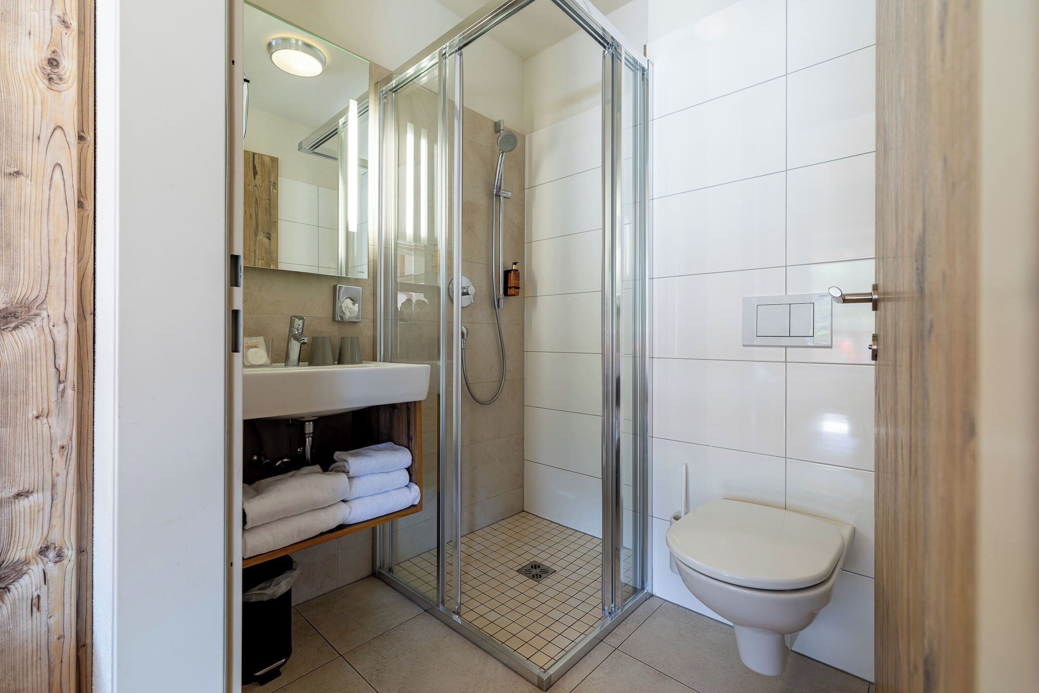 A modern bathroom with a glass shower enclosure, a white toilet, and a sink with a mirror.