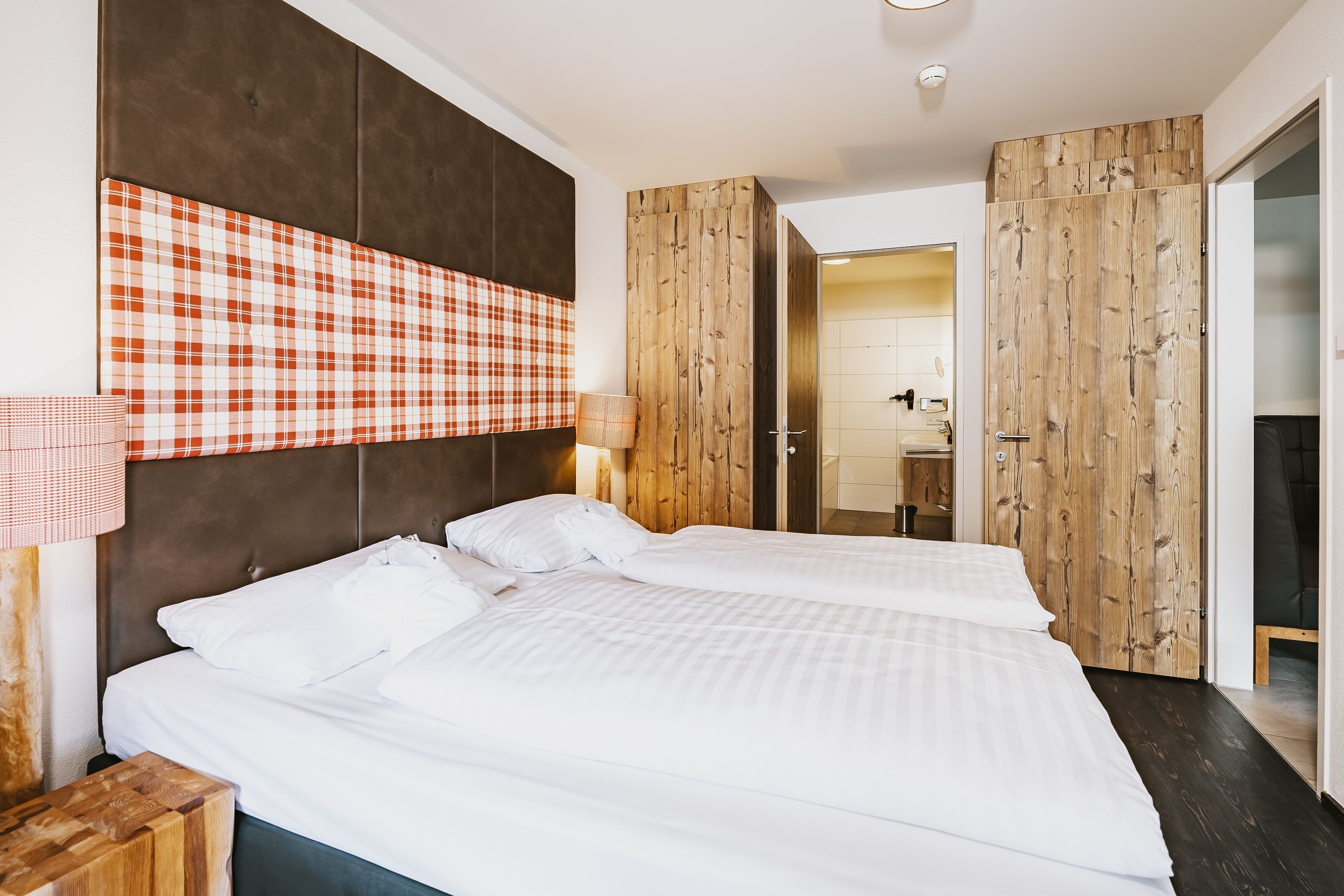 A hotel room with a large bed, a headboard with a plaid pattern, wooden paneling, and a wooden wardrobe.