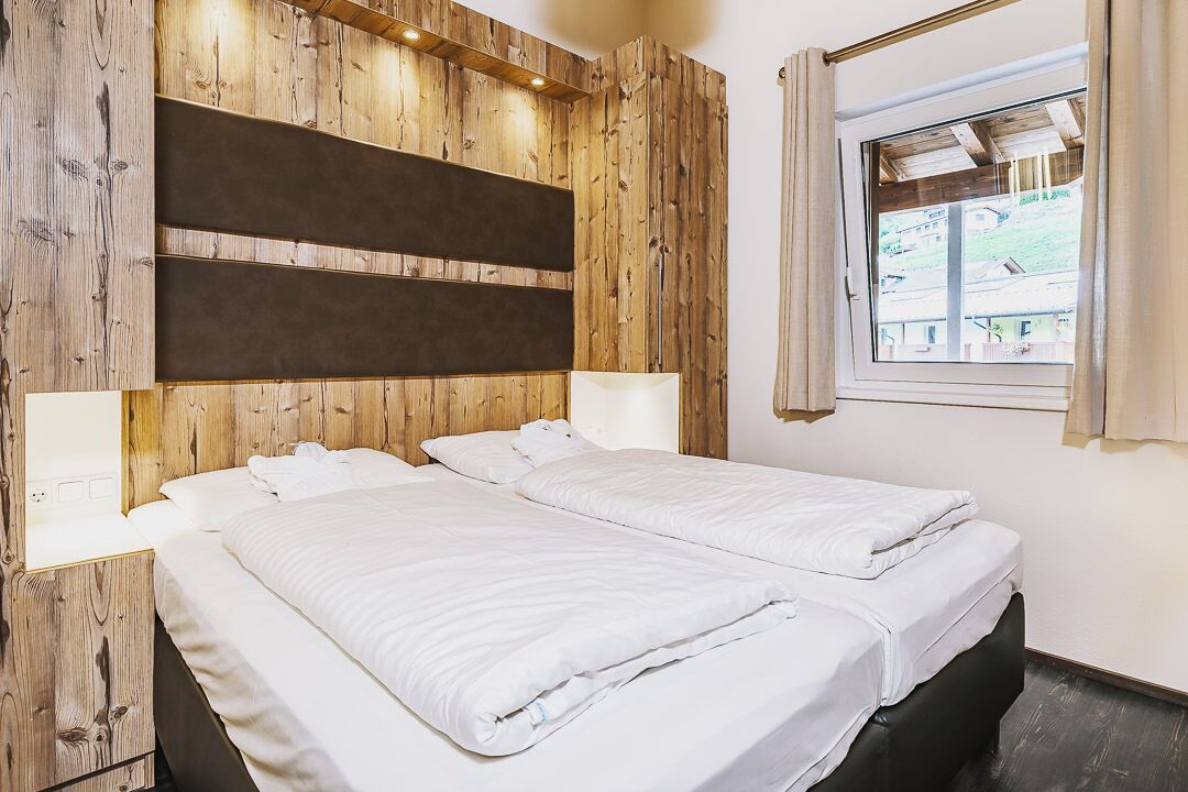 Une chambre avec deux lits, des lambris en bois sur les murs, une fenêtre avec des rideaux et une vue sur l’extérieur.