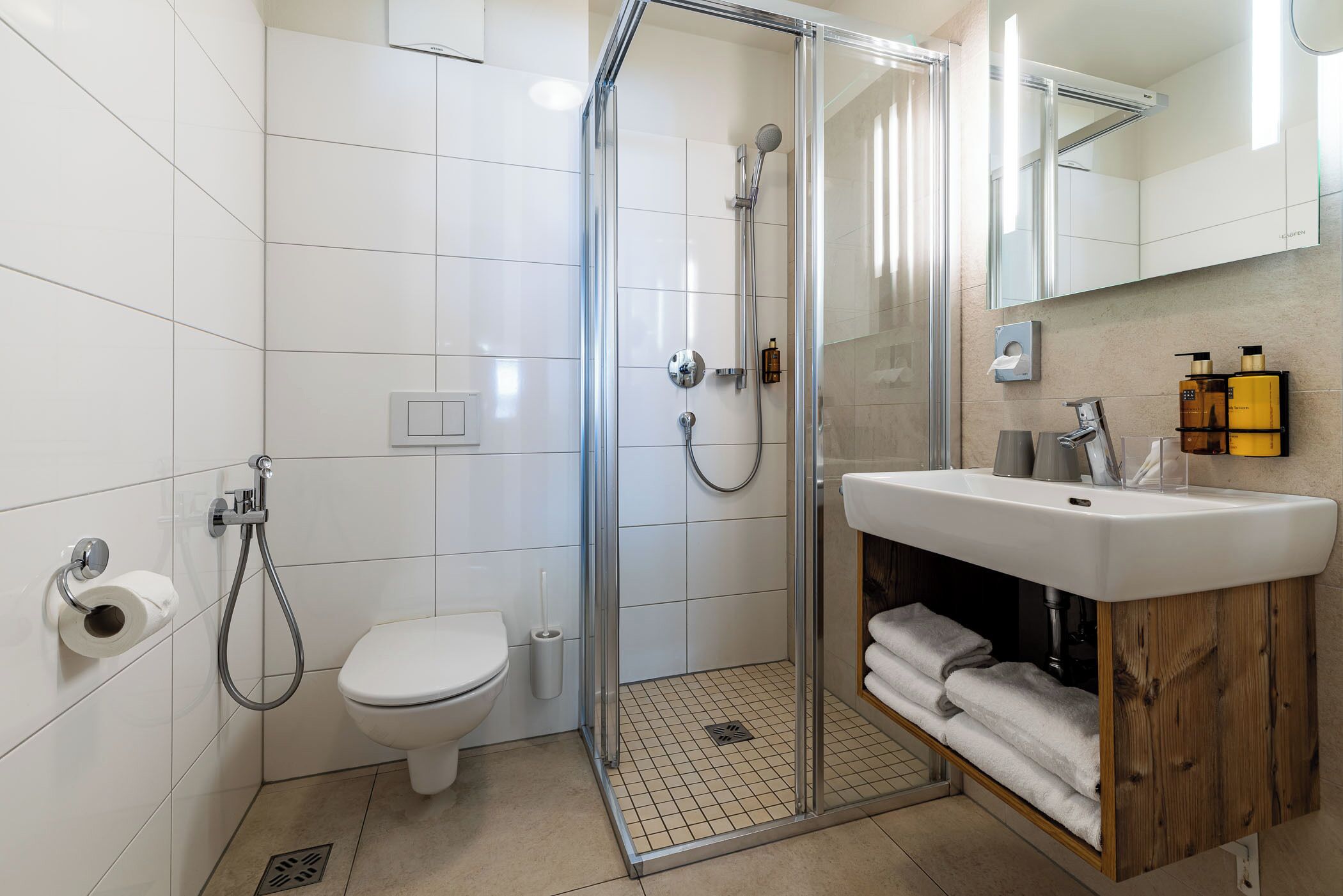 A modern bathroom with a glass-enclosed shower, a white toilet, and a wooden vanity with a sink and towel rack.