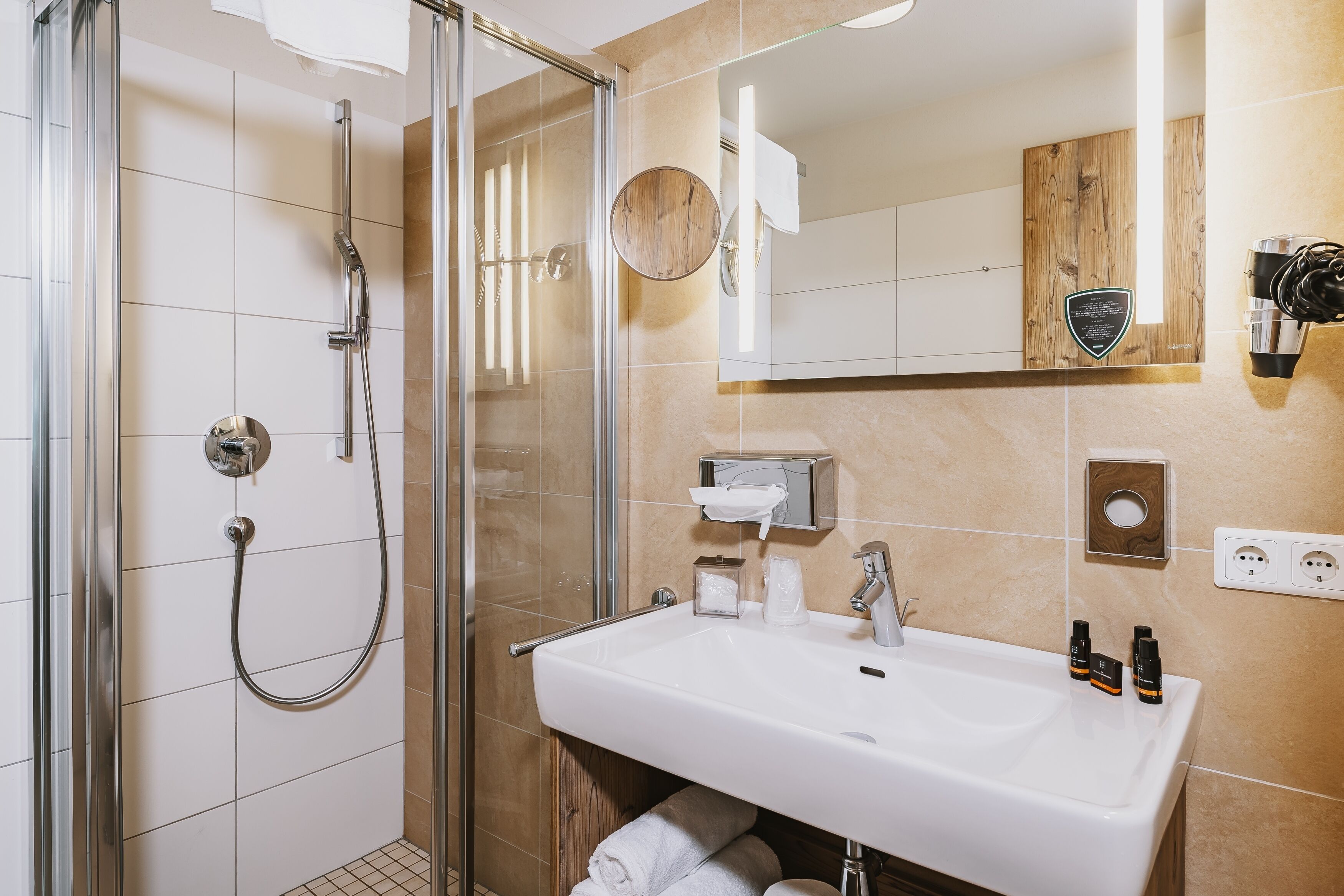 A modern bathroom with a glass-enclosed shower, a white sink, and a wooden vanity.