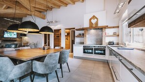Une cuisine moderne avec une table à manger en bois, des chaises grises et des luminaires suspendus.