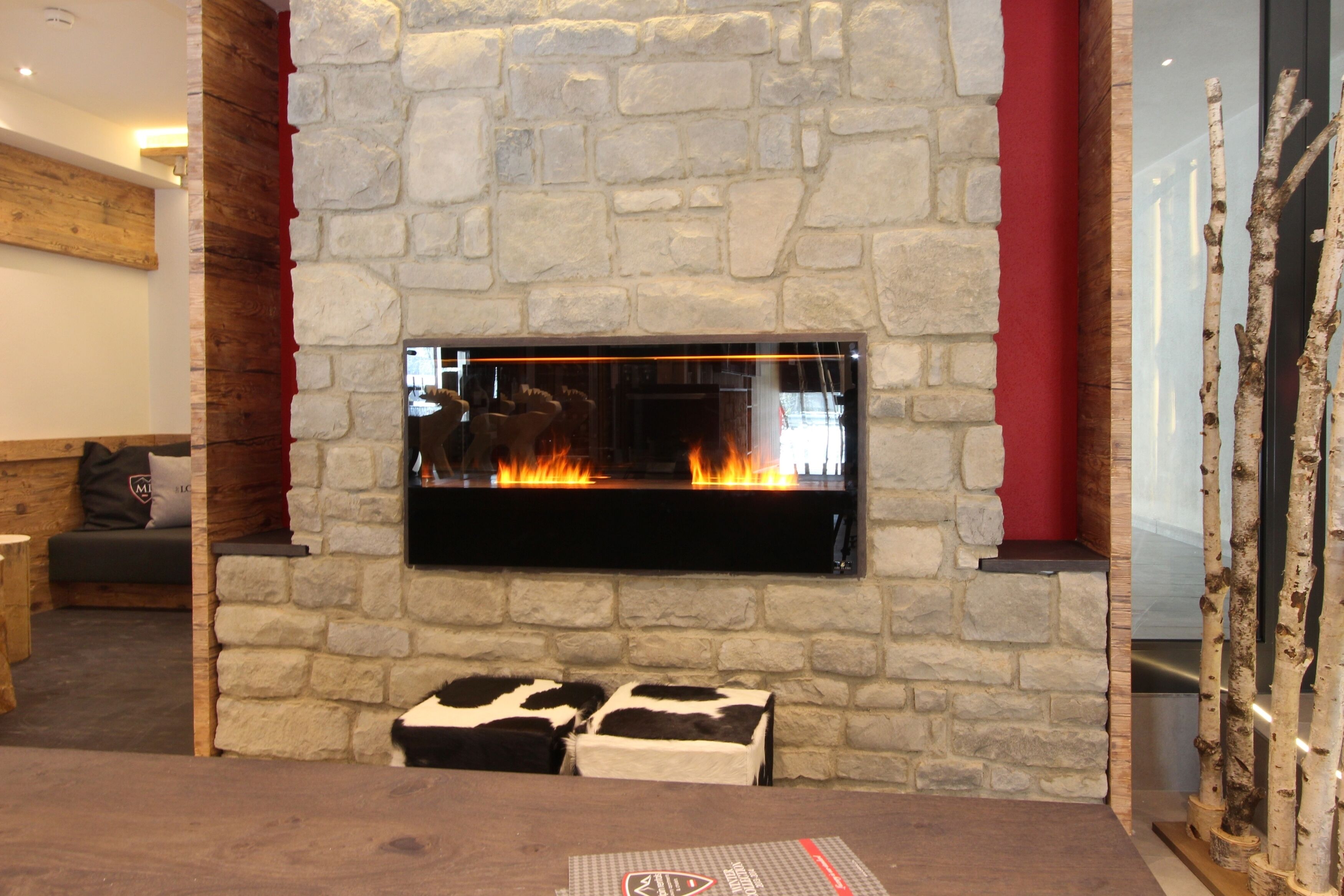 Une cheminée en pierre avec un feu de bois, un banc en bois et un tapis en peau de vache.