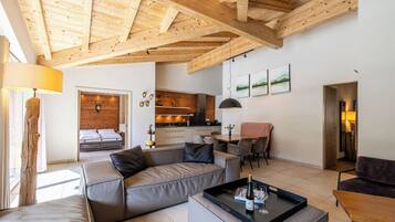 Una sala de estar moderna con techo de madera, un sofá, una mesa de centro y una cocina al fondo.