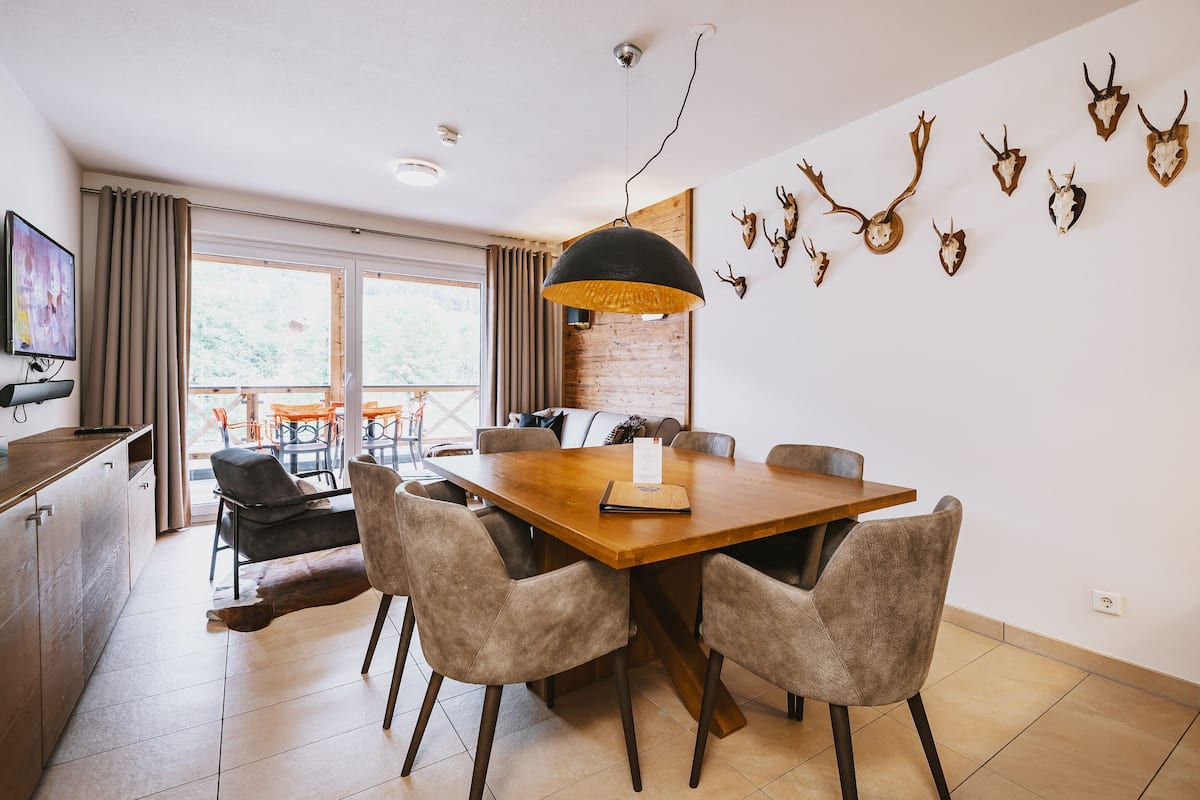 A dining area with a wooden table and four chairs, a pendant light, and a wall-mounted deer head decoration.