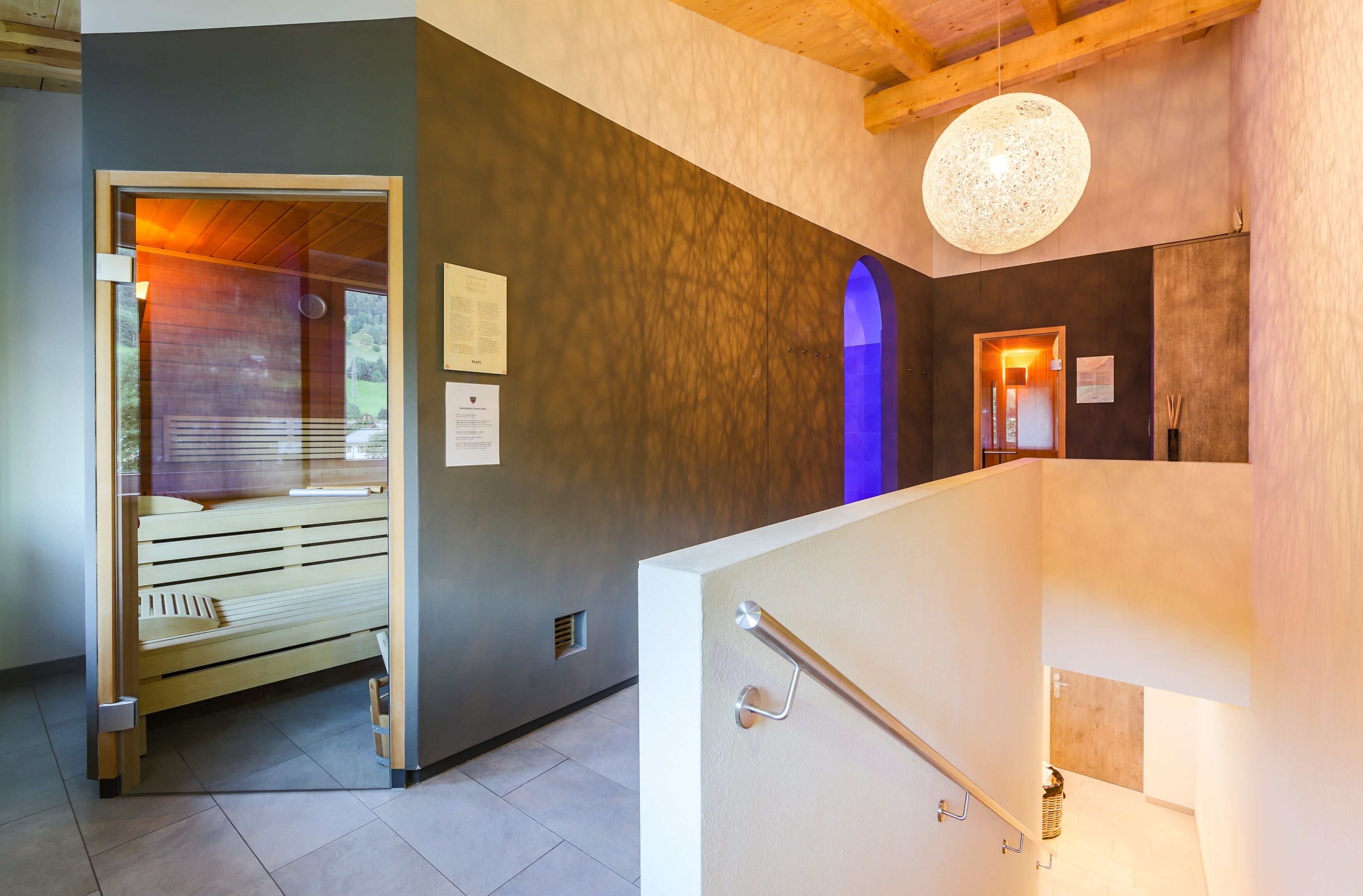 A modern interior with a wooden bench, a textured wall, a hanging light fixture, and a door leading to another room.