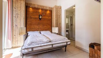Een slaapkamer met een houten hoofdbord, een bed met wit beddengoed, een bedlampje en een houten kist.