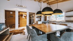 Une cuisine moderne avec des meubles en bois, un coin repas doté d’une table en bois et de chaises grises, ainsi que des luminaires suspendus.