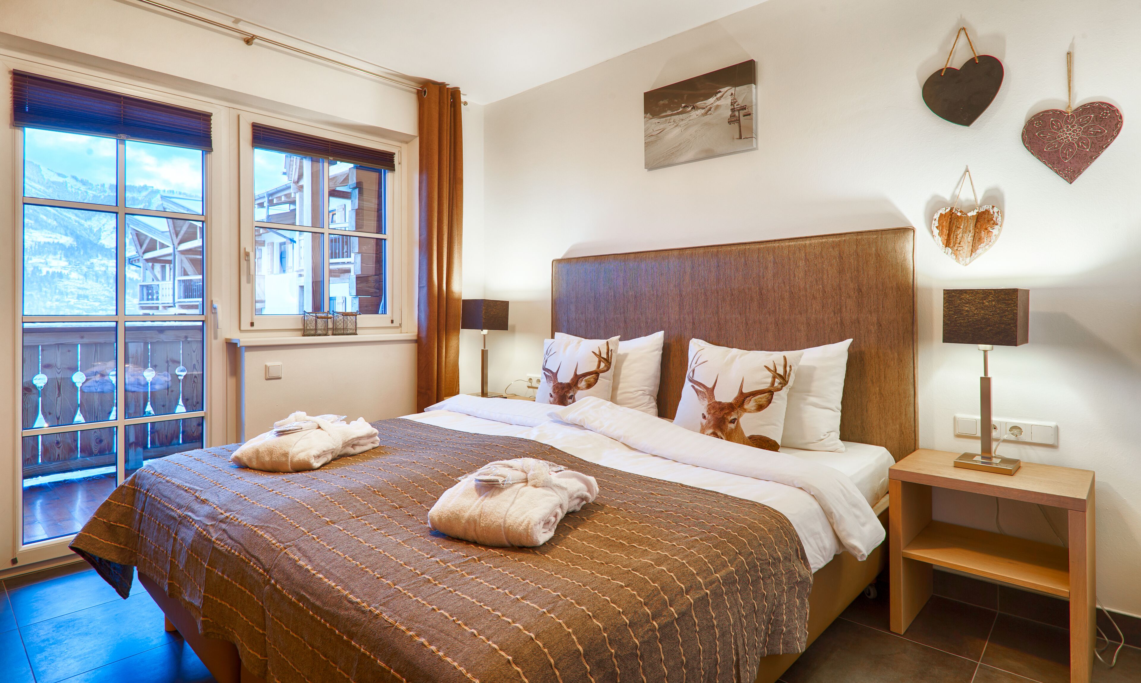 A hotel room with a large bed, two pillows with deer prints, a bedside table with a lamp, and a window with a view of a building.