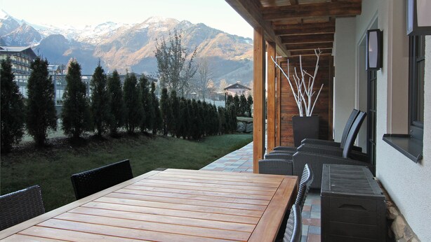 A wooden table and chairs on an outdoor patio with a mountain view. - AvenidA Mountain Resort by Alpin Rentals - incl Summercard (Kaprun)