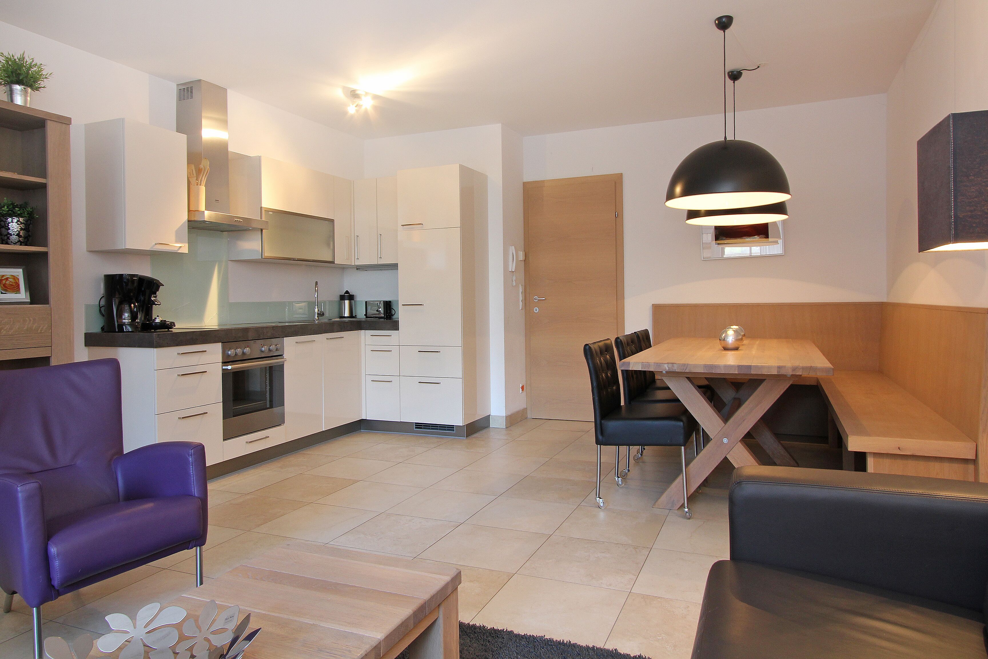 Een moderne keuken met witte kasten, een eettafel met stoelen en een paarse fauteuil.