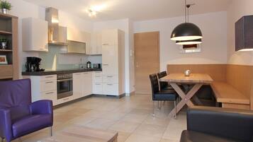 Een moderne keuken met witte kasten, een eettafel met stoelen en een paarse fauteuil.