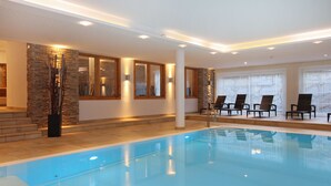 A modern indoor swimming pool with clear blue water, surrounded by stone walls and wooden-framed windows. - AvenidA Mountain Resort by Alpin Rentals - incl Summercard (Kaprun)