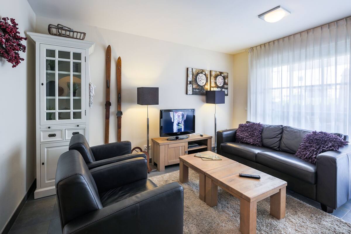 Moderni olohuone, jossa on sohva, sohvapöytä, televisio ja kaappi.
