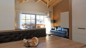 A modern kitchen with a wooden table, a decorative shell, and a view of a dining area with a sofa and a window. - AvenidA Mountain Resort by Alpin Rentals - incl Summercard (Kaprun)