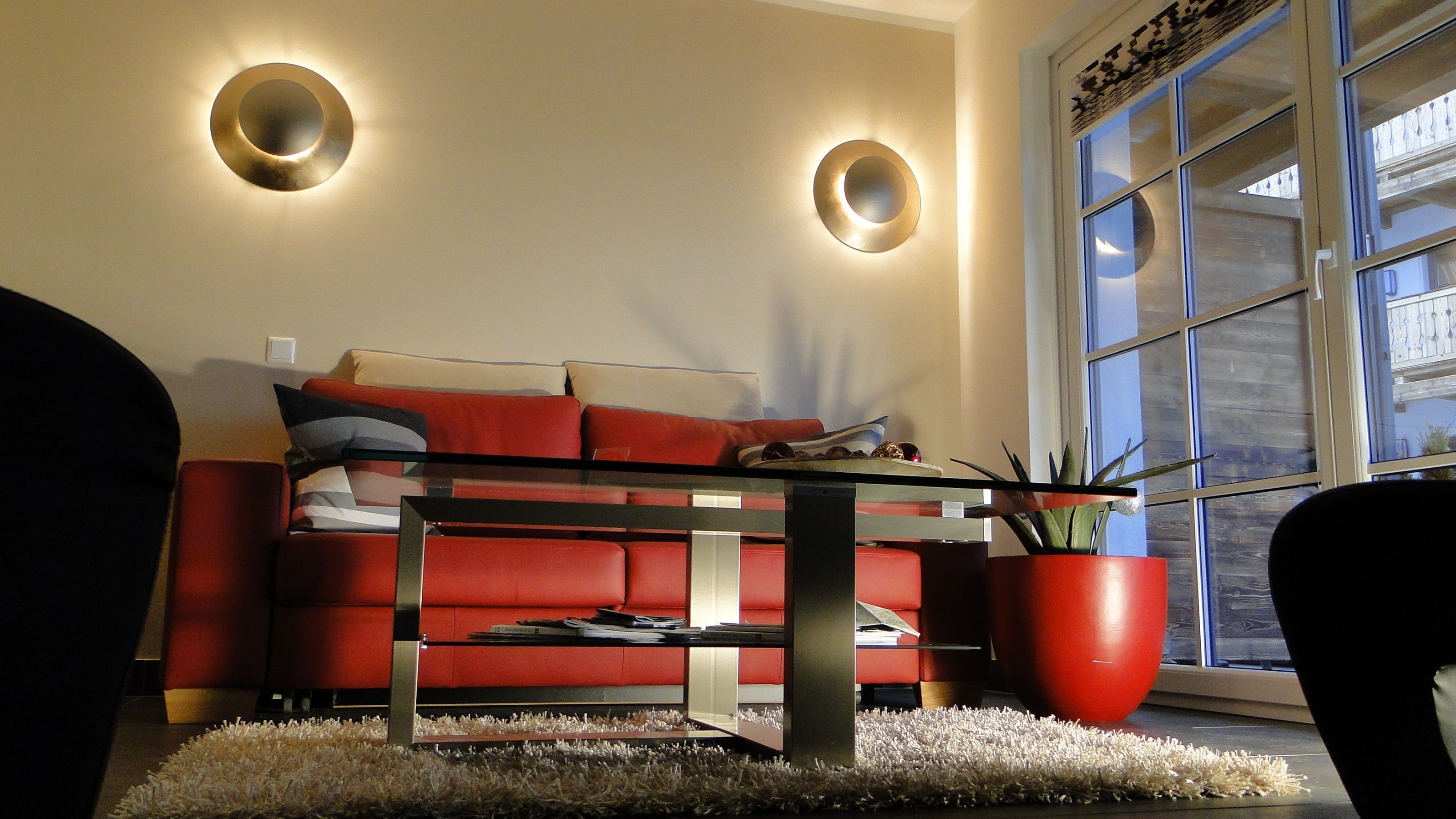 A modern living room with a red sofa, a glass coffee table, and two wall-mounted lights.