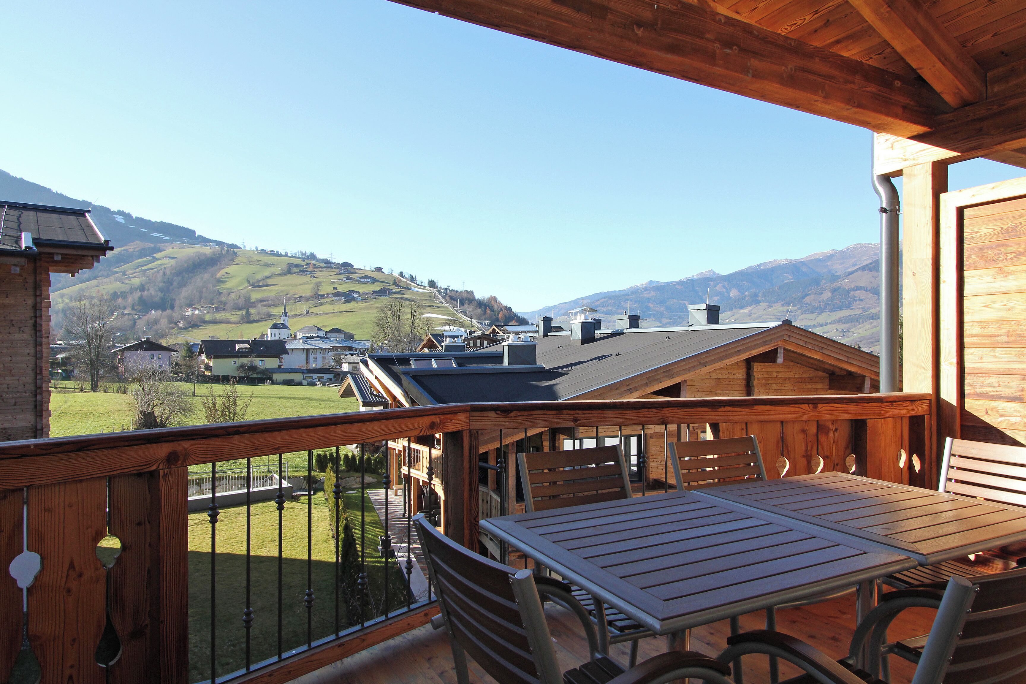 Una terraza de madera con una mesa y sillas, con vistas a un valle con casas y montañas.