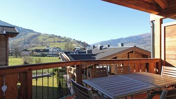 Una terraza de madera con una mesa y sillas, con vistas a un valle con casas y montañas.