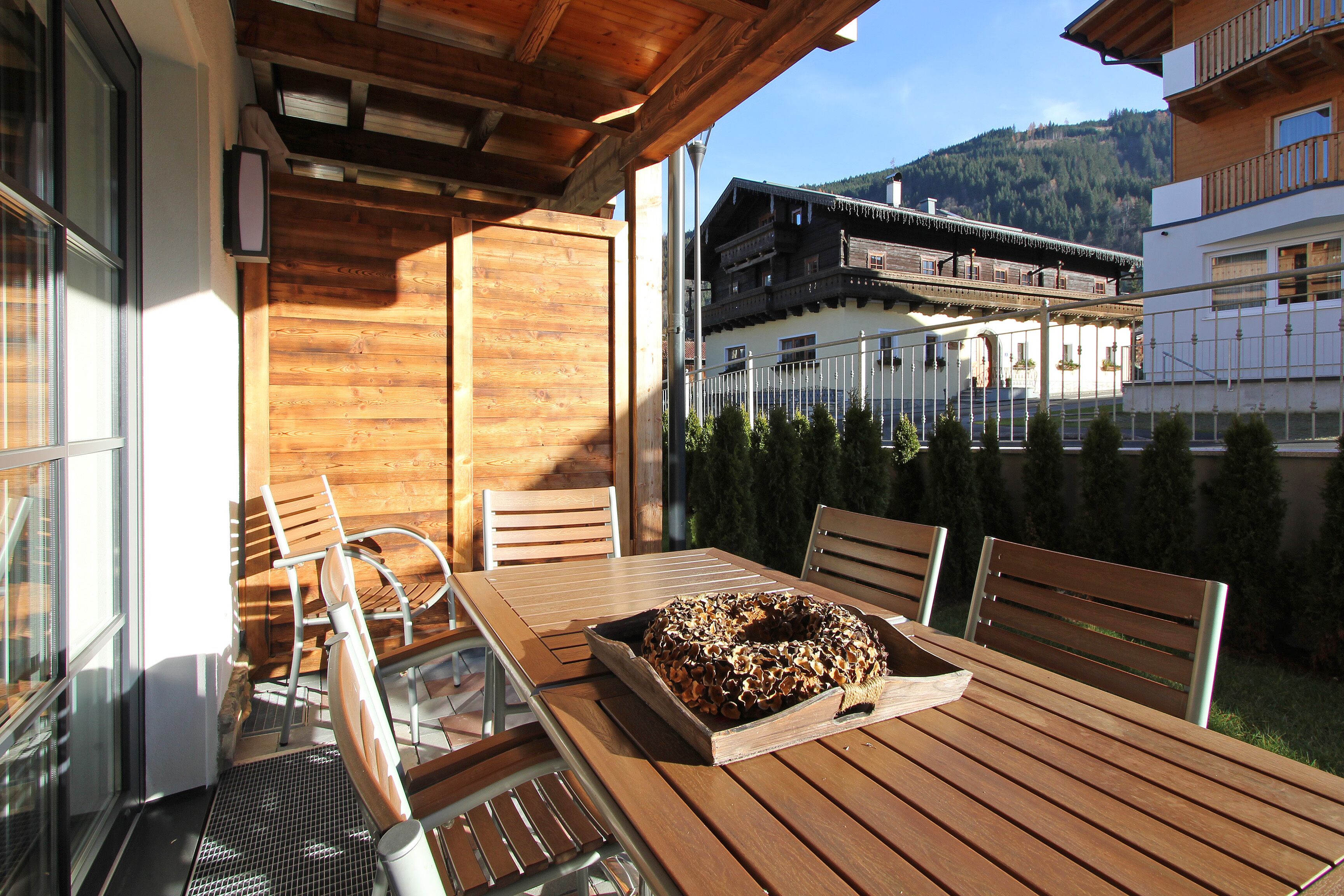 A wooden table with a tray of food, chairs, and a view of a mountain and buildings.