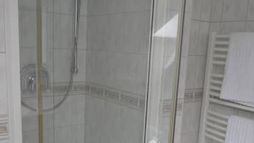 A glass-enclosed shower stall with a handheld showerhead and a wall-mounted faucet.