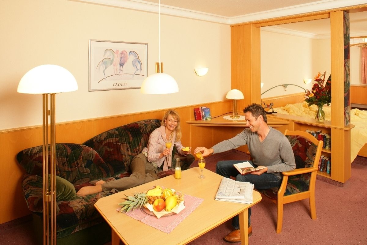 Ein gemütliches Zimmer mit einer Holzsofa, einem kleinen Tisch mit Obst und Getränken, und einem Mann, der ein Buch liest.