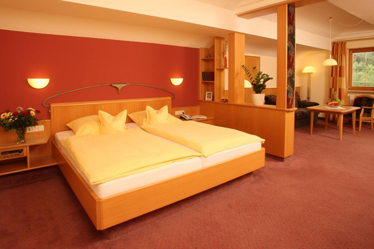 Hotellihuone, jossa on suuri sänky, työpöytä, tuoli, pieni pöytä, peili ja ikkuna, jossa on verhot.