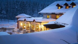 Un edificio cubierto de nieve con numerosas ventanas y una cálida luz en su interior.