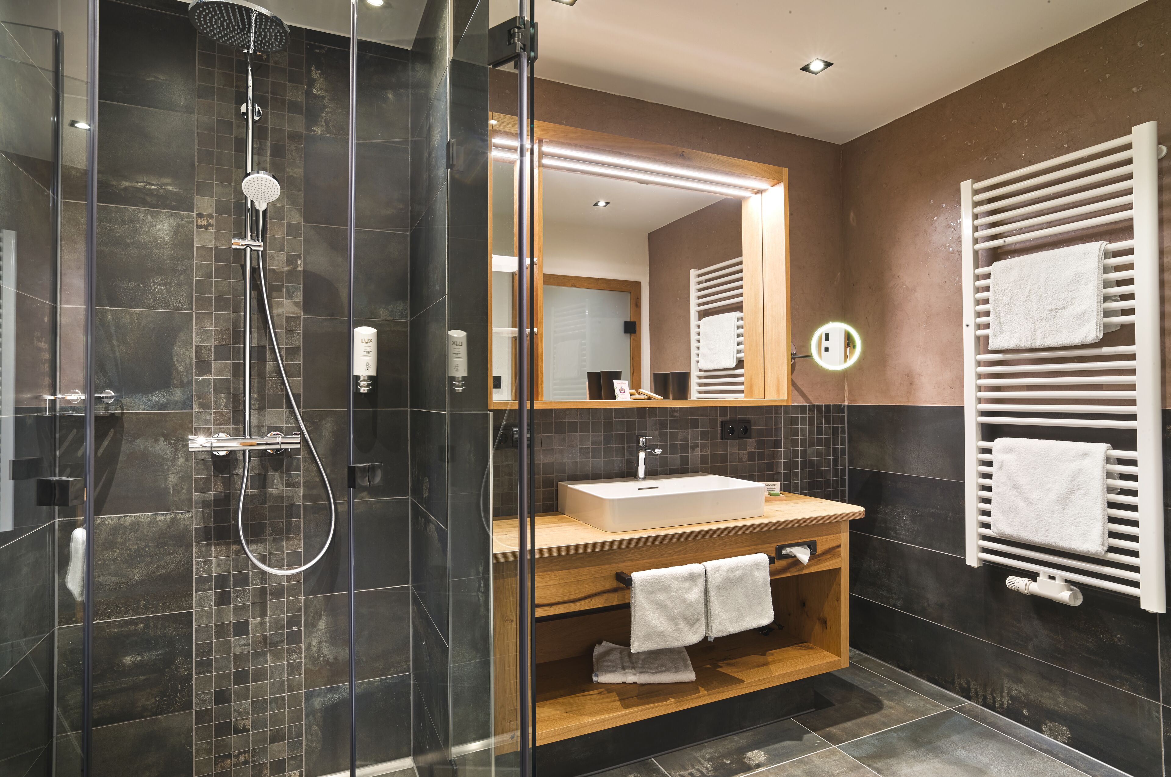 Un bagno moderno con doccia vetro, mobile bagno in legno, uno specchio grande e un portasciugamani.