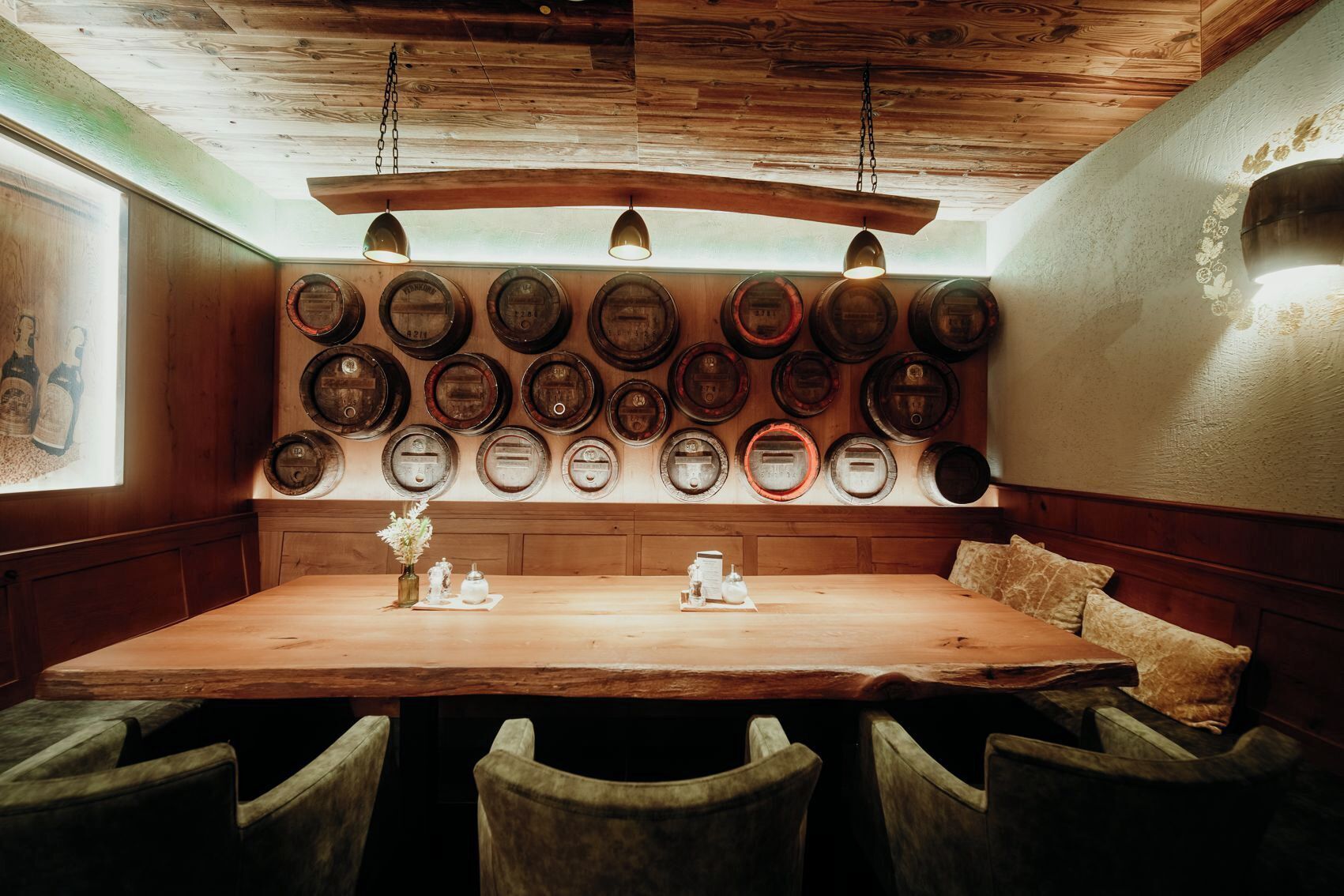 A wooden dining table with a bench, surrounded by chairs, and a wall of vintage beer barrels.