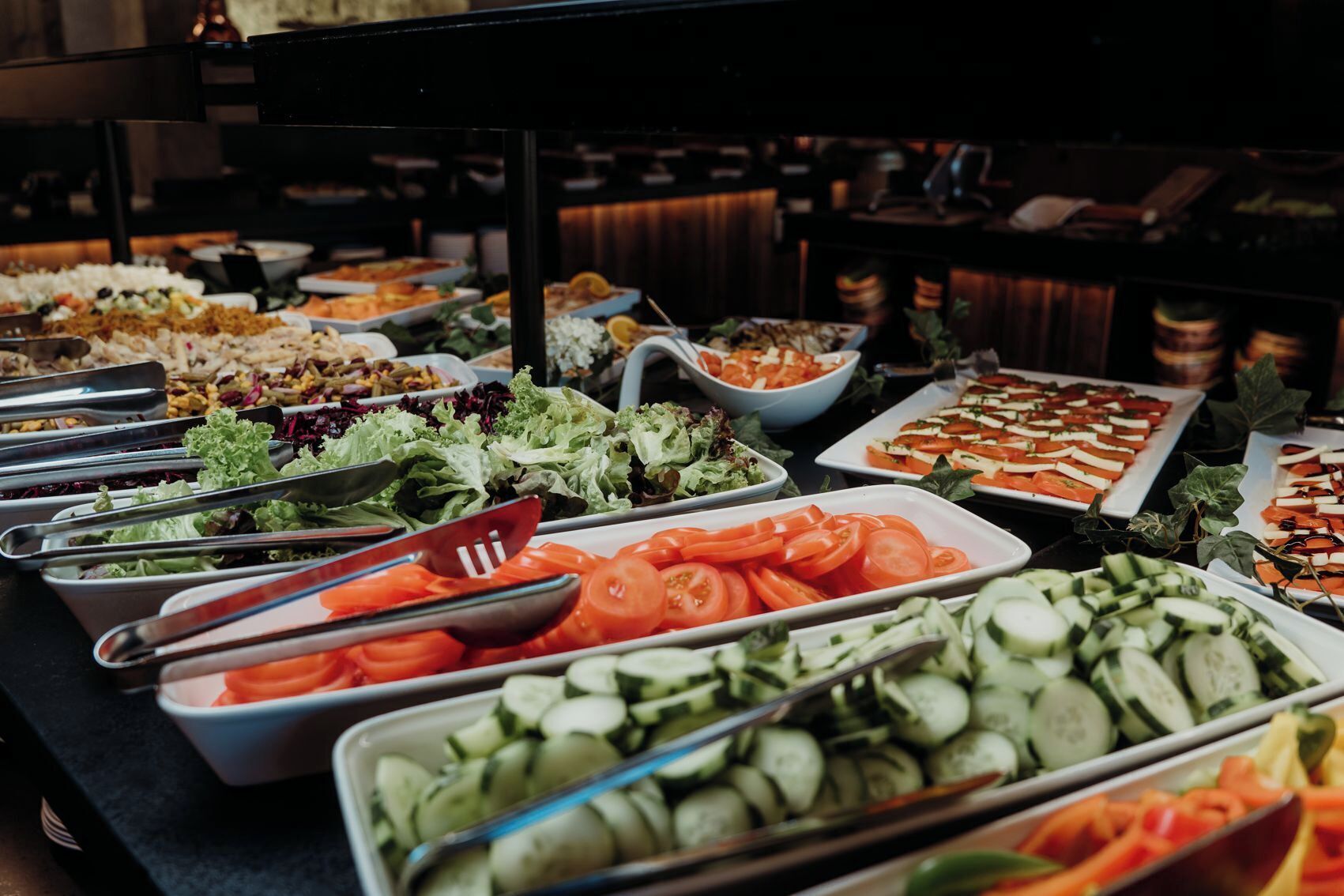 A buffet with various food options including salads, sliced tomatoes, cucumbers, and other vegetables.