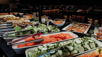 A buffet with various food options including salads, sliced tomatoes, cucumbers, and other vegetables.
