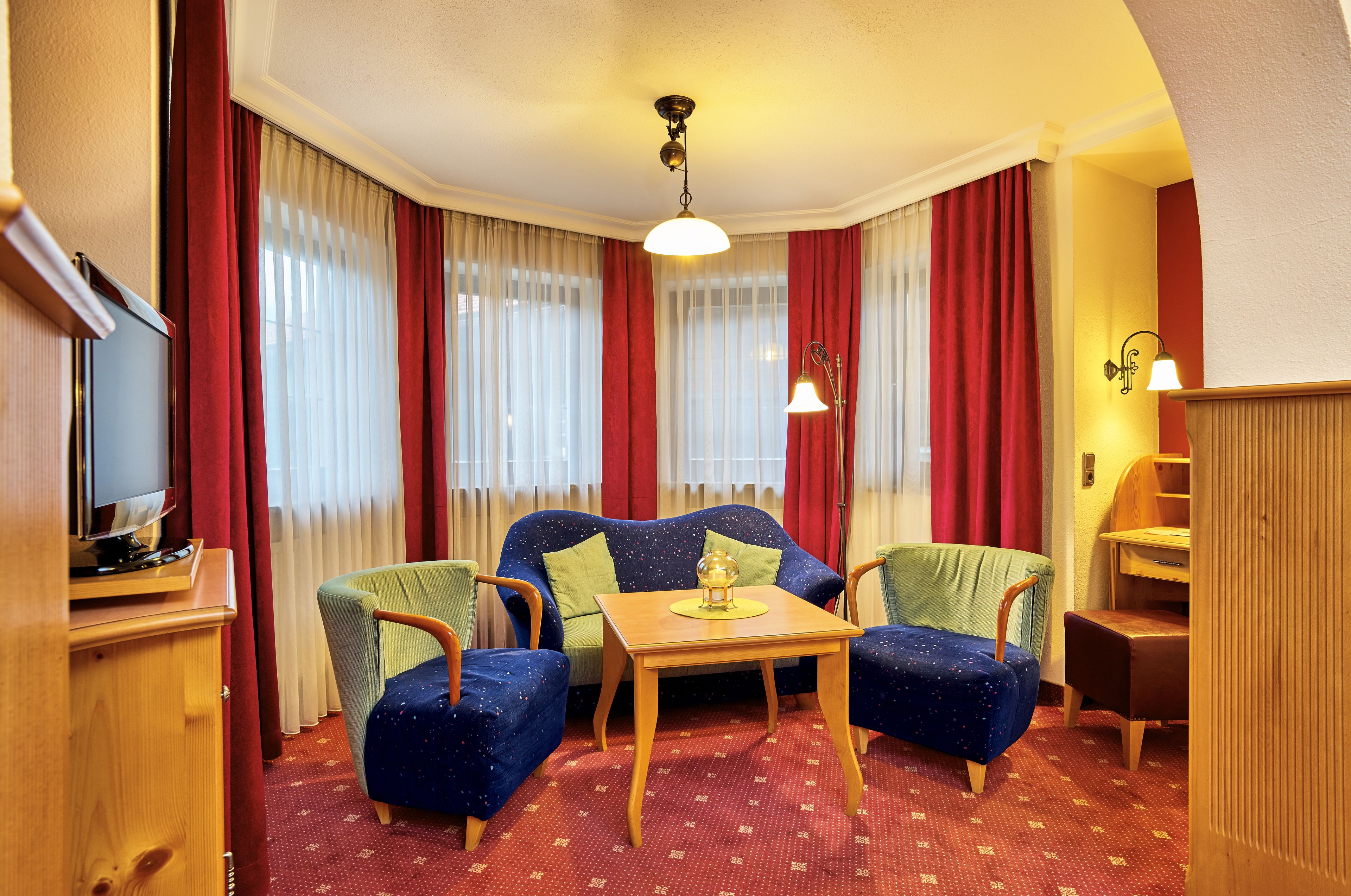 A hotel room with a blue sofa, two armchairs, a wooden table, and a television on a wooden cabinet.