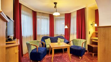 A hotel room with a blue sofa, two armchairs, a wooden table, and a television on a wooden cabinet.