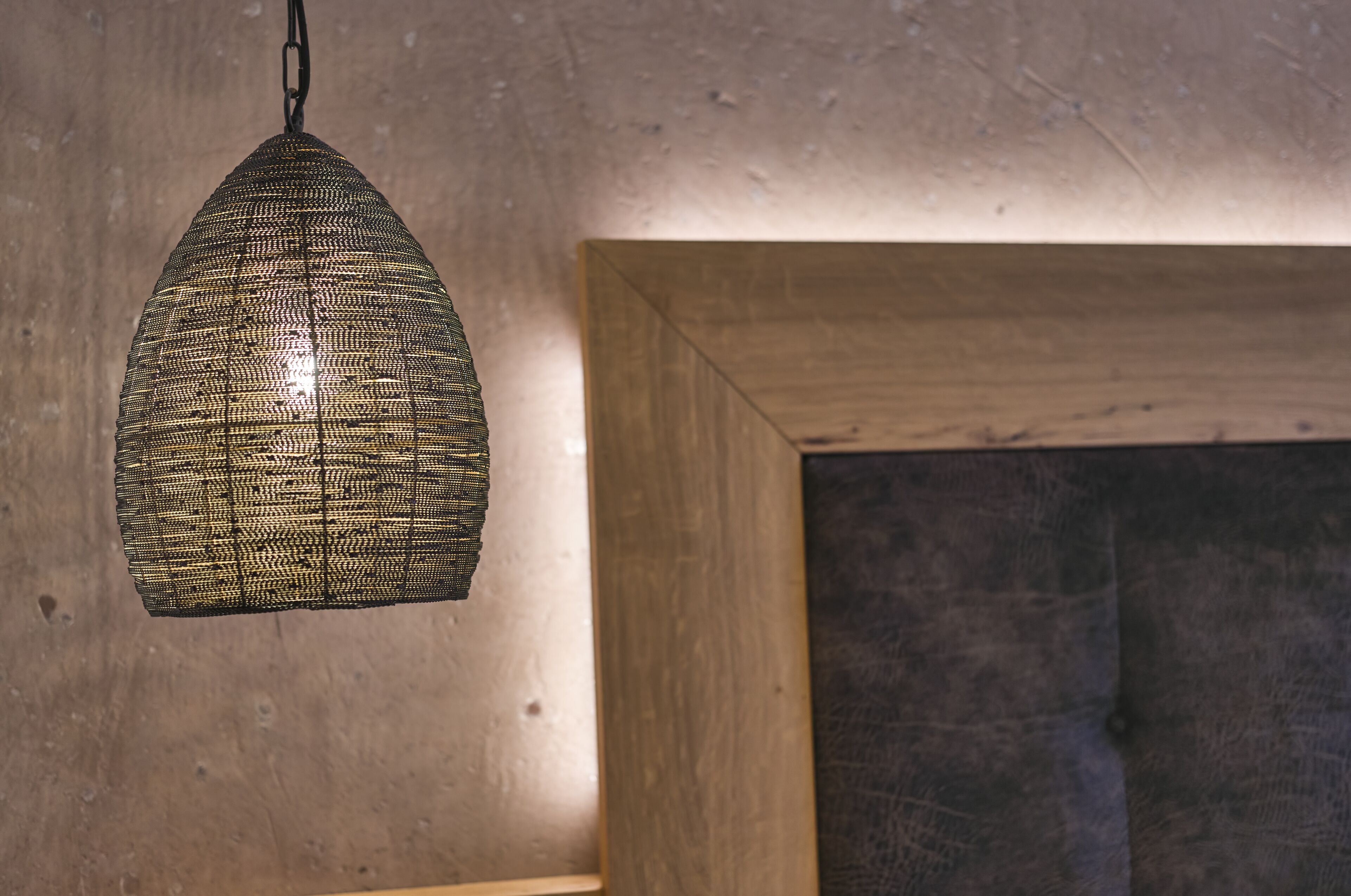Un luminaire suspendu à motifs dans une pièce dotée de poutres en bois et d’un mur en béton.
