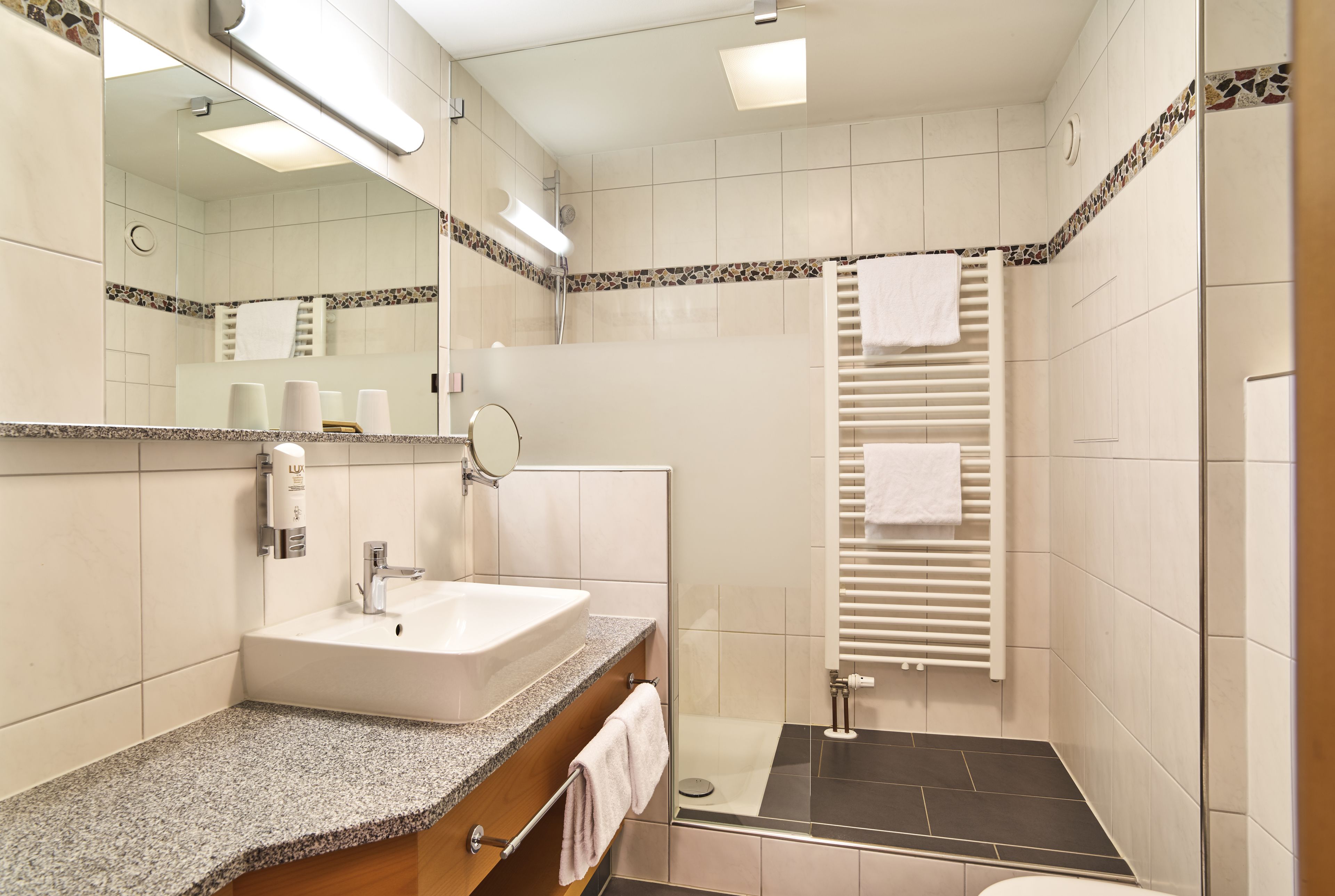 A modern bathroom with a granite countertop, a white sink, a glass shower enclosure, and a tiled shower floor.