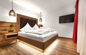 A modern bedroom with a wooden headboard, a flat-screen TV, and a bedside table with a lamp.