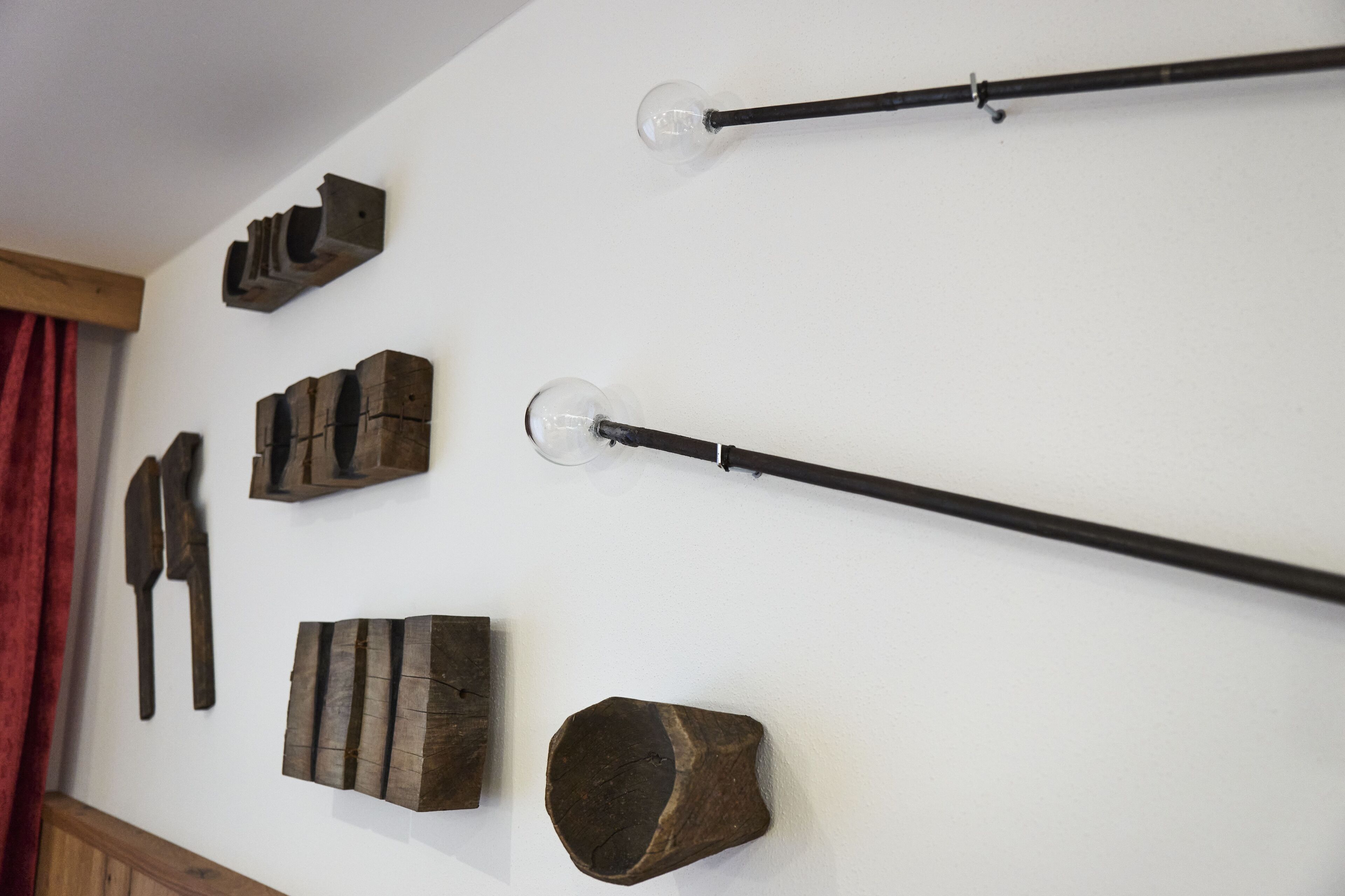 A wall with various wooden objects, including a long black rod with a glass bulb at the end, a wooden block with a handle, and several other wooden items.