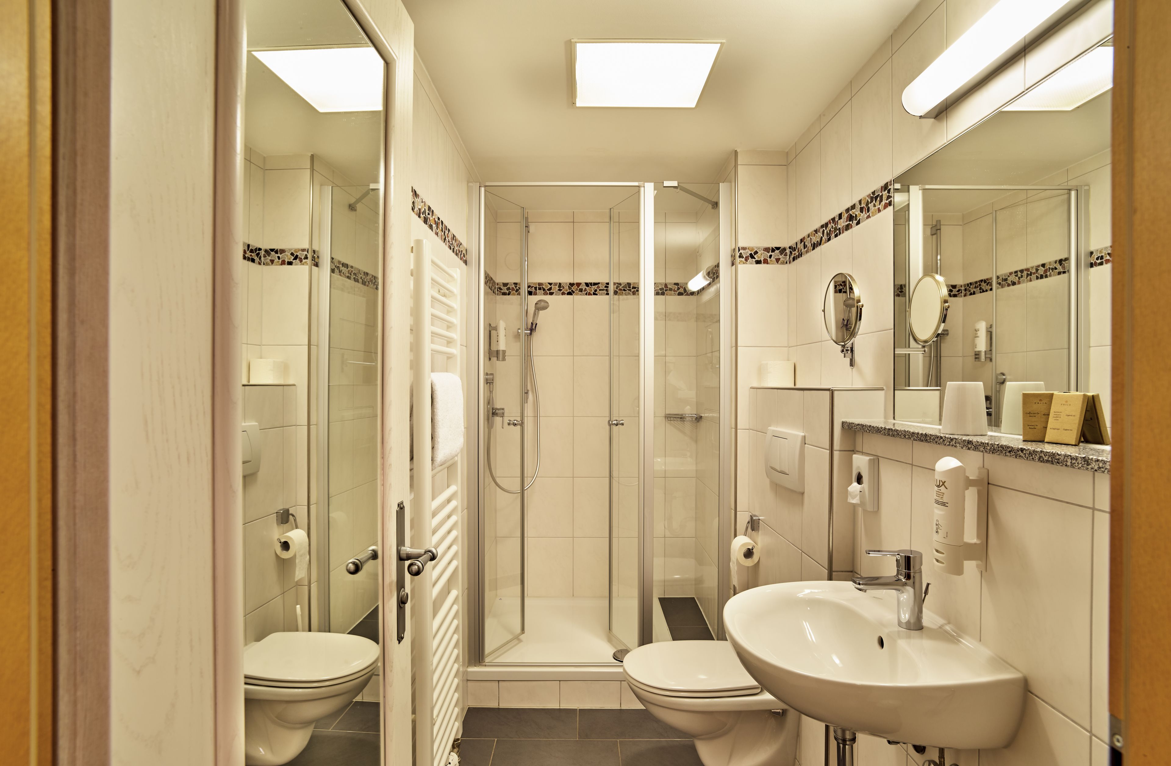 A modern bathroom with a glass-enclosed shower, two toilets, a sink, and a mirror.