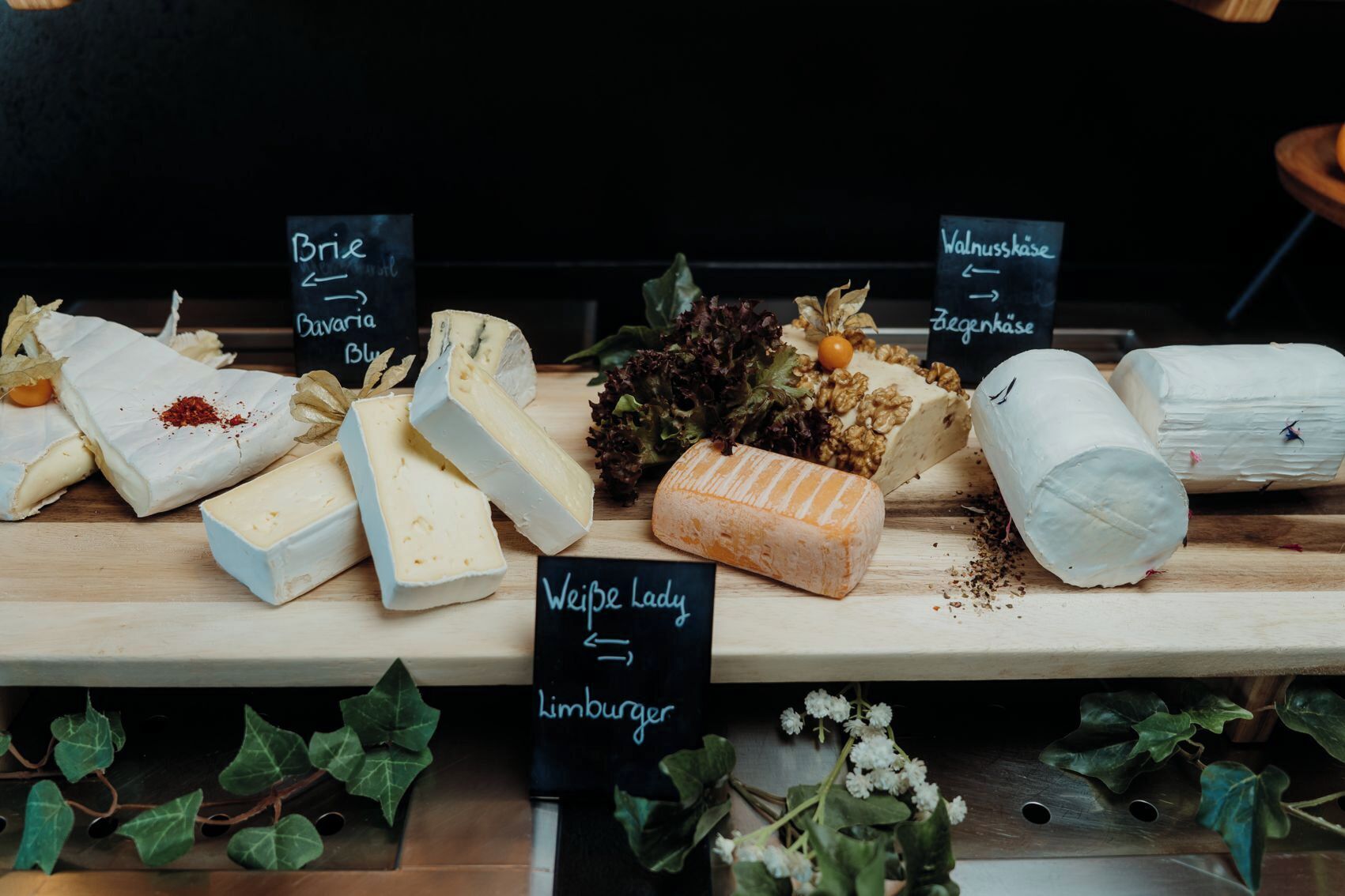 A variety of cheeses on a wooden board with labels indicating different types.