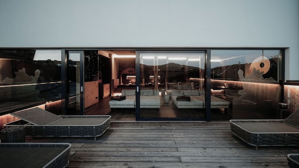 Een modern interieur met een glazen wand, een houten terras en een zitgedeelte buiten.