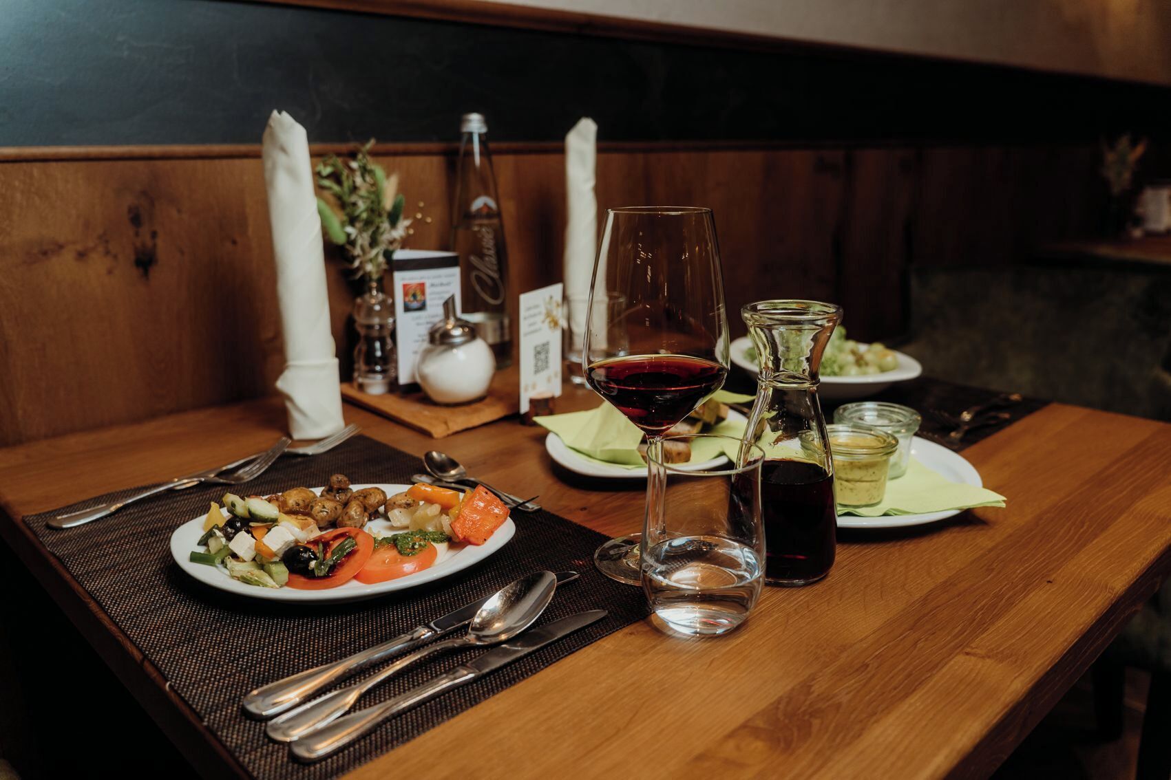 A wooden table with a plate of food, a glass of red wine, and a bottle of olive oil.