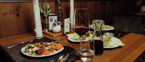 A wooden table with a plate of food, a glass of red wine, and a bottle of olive oil.