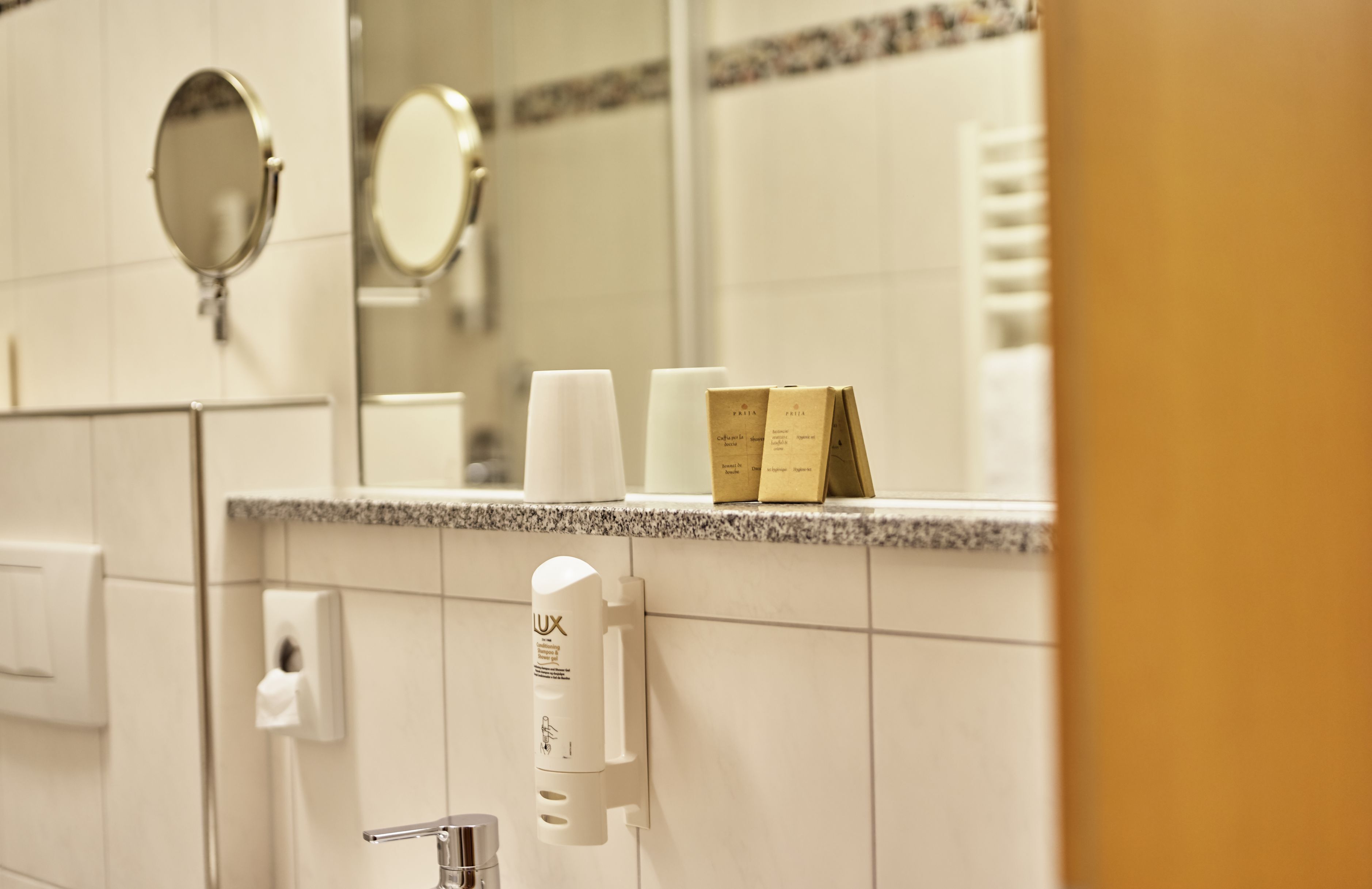 A bathroom with a mirror, a towel rack, a paper towel dispenser, and a soap dispenser.