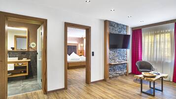 Ein modernes Hotelzimmer mit Holzboden, einer Wand mit Steinakzenten, einem Flachbildfernseher, einem gemütlichen Bett, einer Holzbank mit Schale und einem großen Fenster mit Vorhängen.