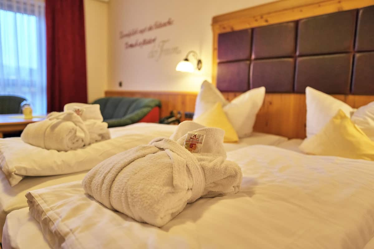 Une chambre d’hôtel avec deux lits, chacun agrémenté de serviettes et d’oreillers pliés. On peut voir une lampe fixée au mur et un panneau avec du texte.